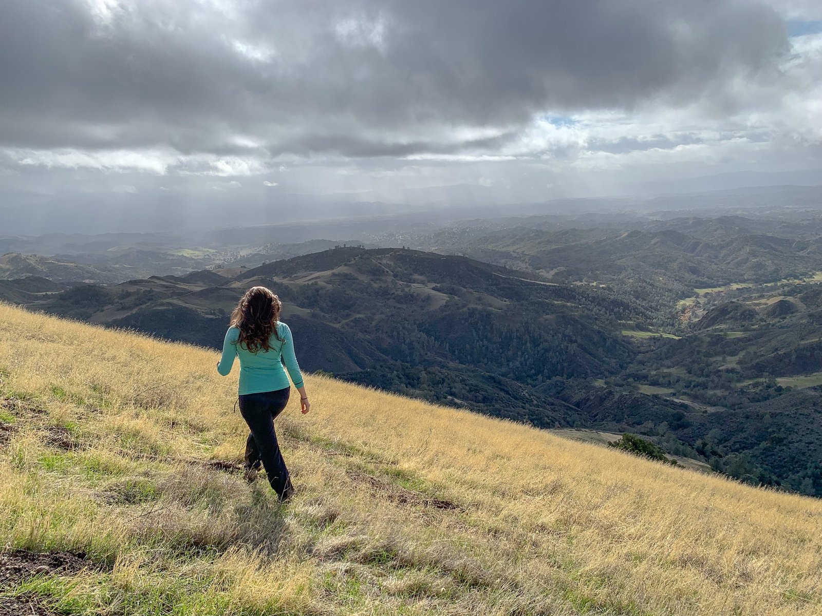 woman walking through grass field overlooking mountain