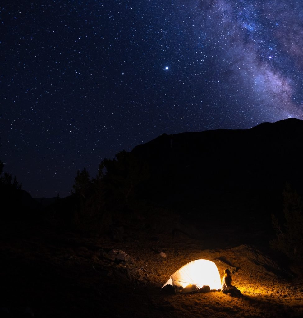 woman sitting by tent under milky way while camping