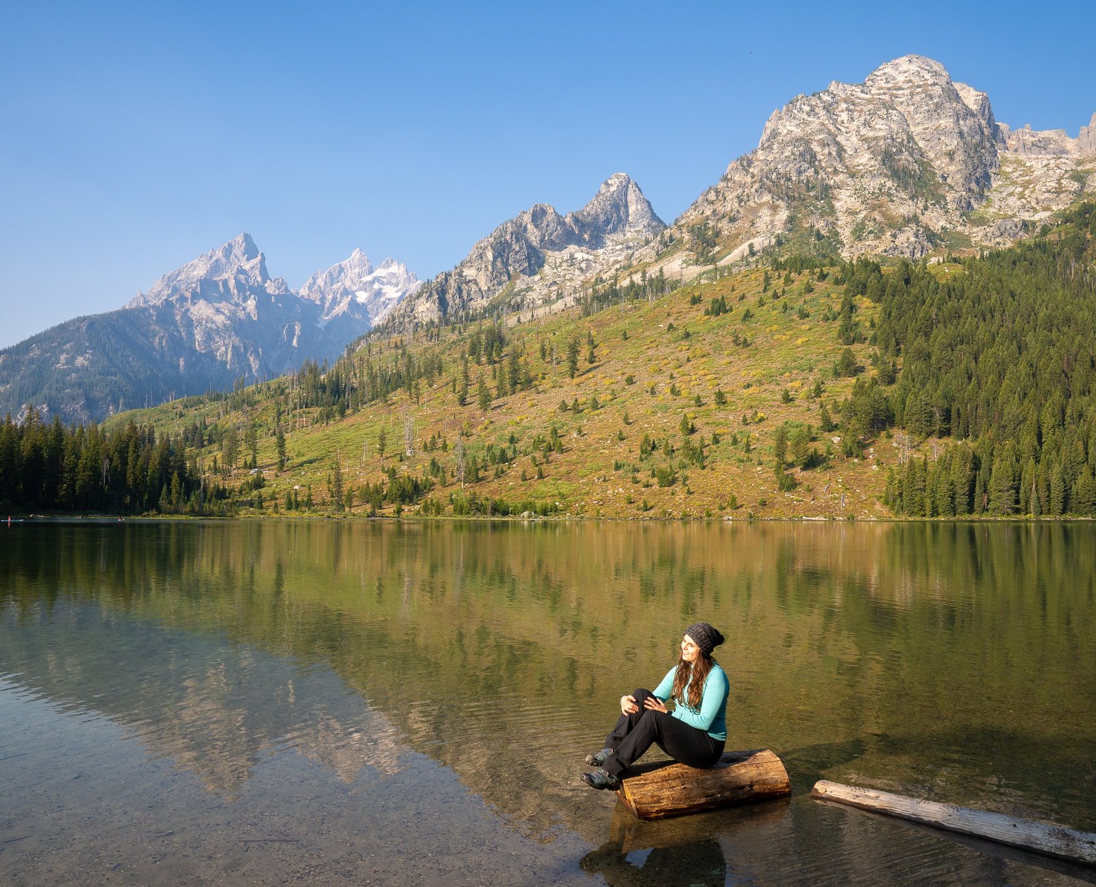 woman sitting by lake in grand tetons national park at jenny lake