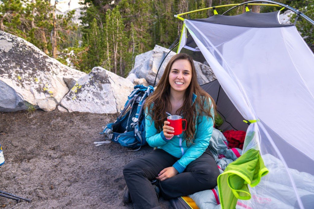 woman sitting in tent on a backpacking trip with a mug