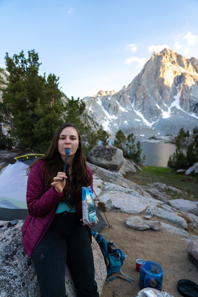 woman eating a freeze dried meal while camping in the mountains