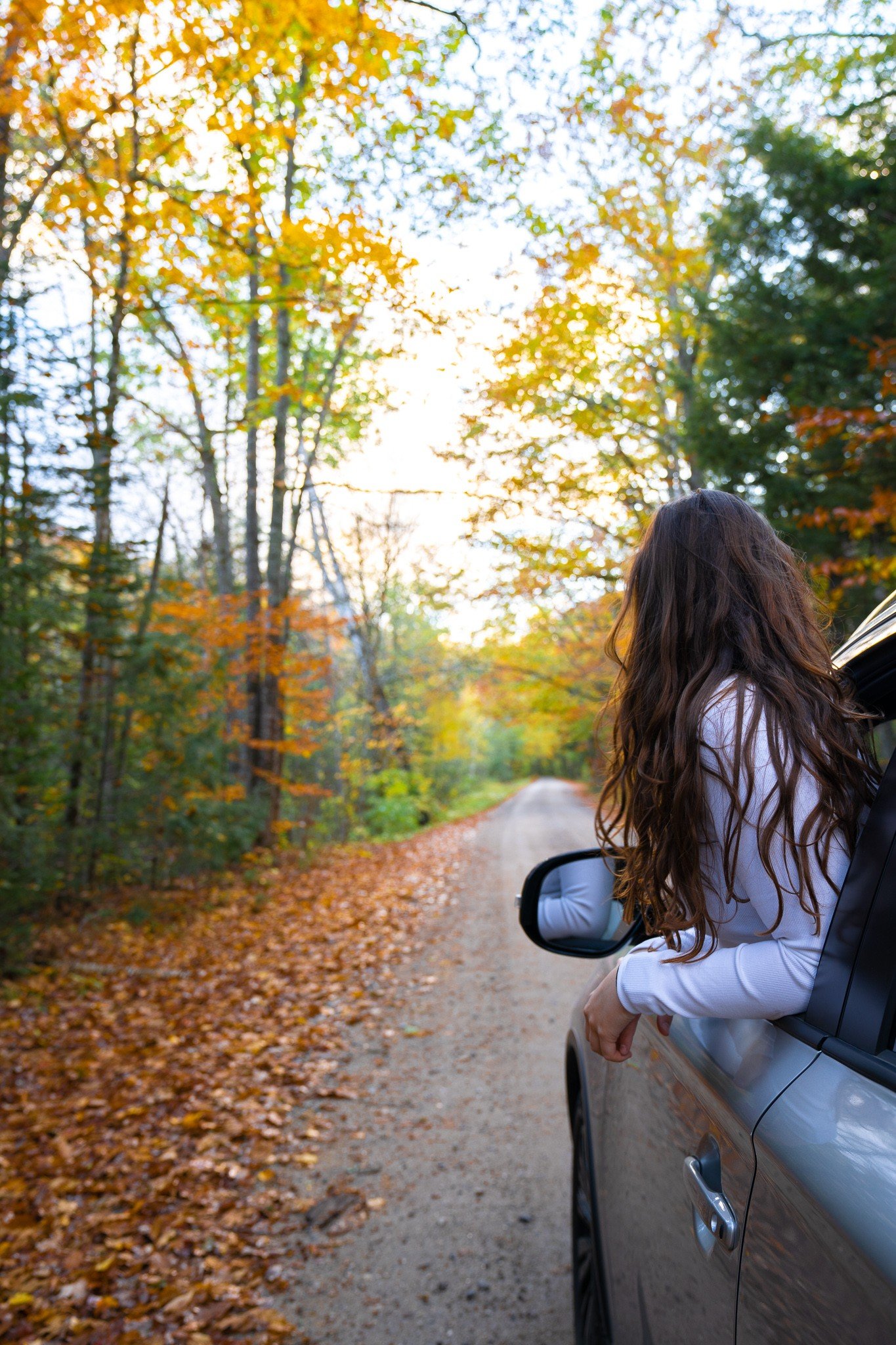 woman in car on a dirt road with fall foliage