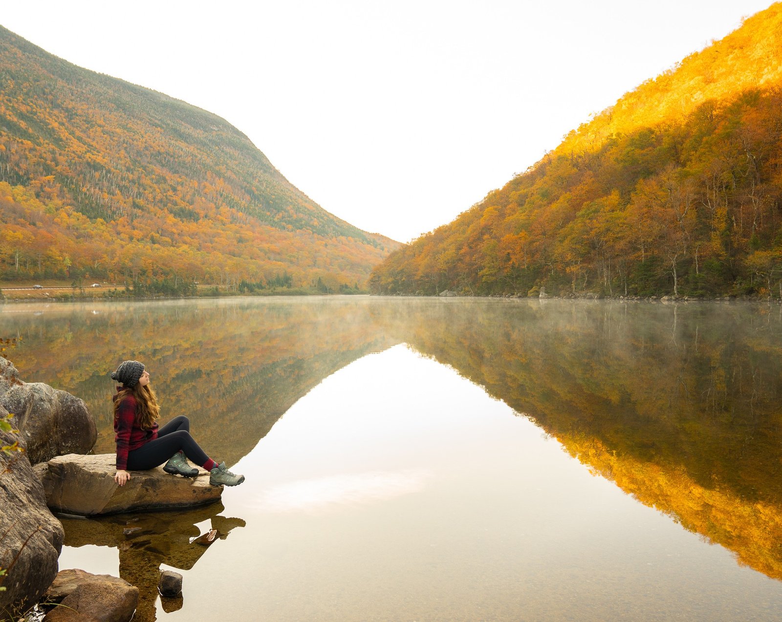 woman sitting by a lake with fall foliage